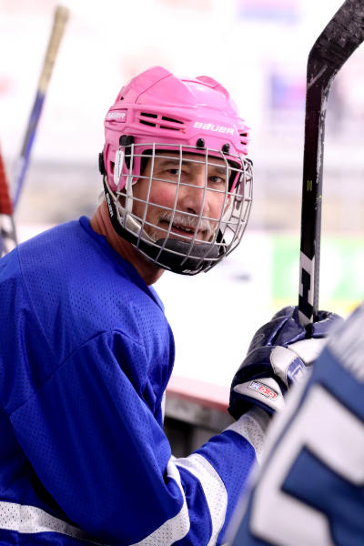 Image of hockey player sitting on the bench with teammates, smiling at the camera.